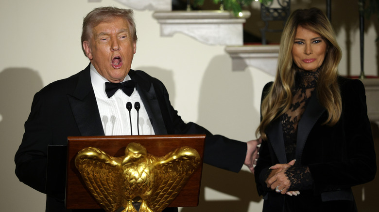 Donald Trump with mouth open at podium while gesturing to Melania