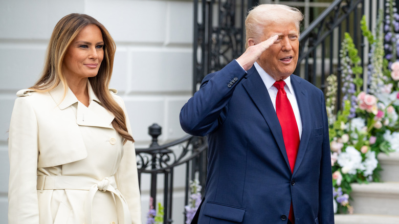 Melania Trump looks straight ahead as Donald Trump does a salute next to her