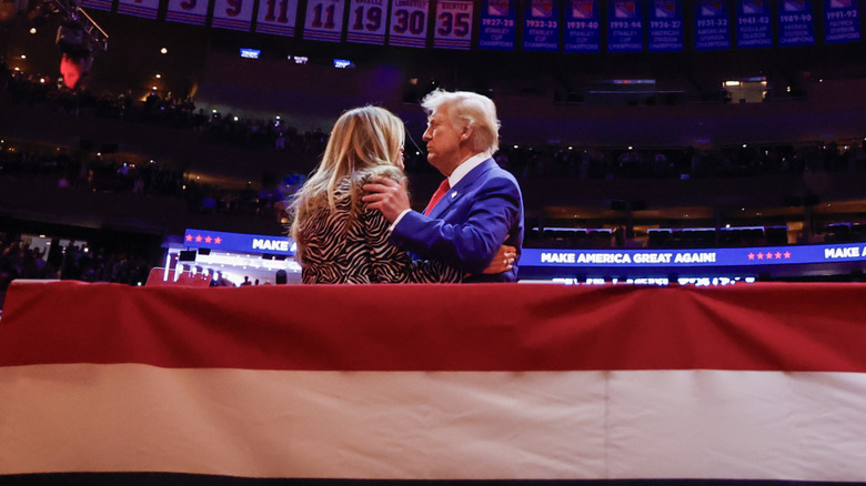 Donald Trump holding Melania Trump's shoulders tightly on stage at a rally
