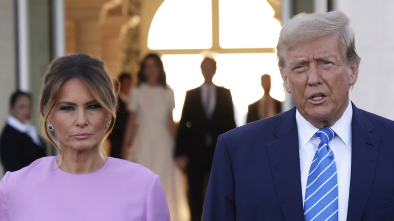 Melania Trump scowling next to Donald Trump as he talks