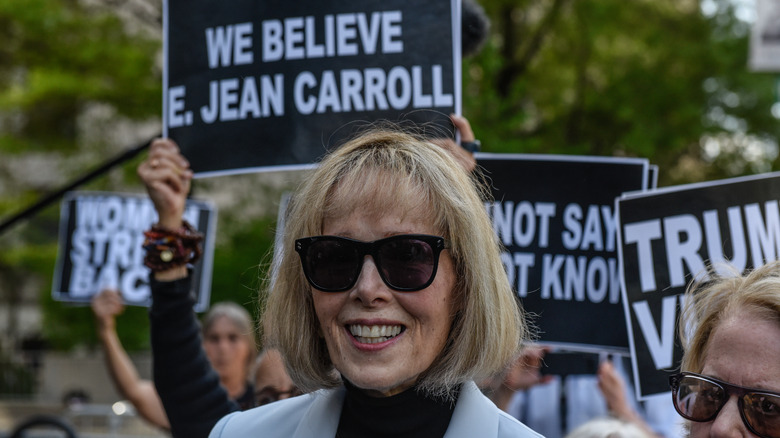 E. Jean Carroll sunglasses while supporters carry signs