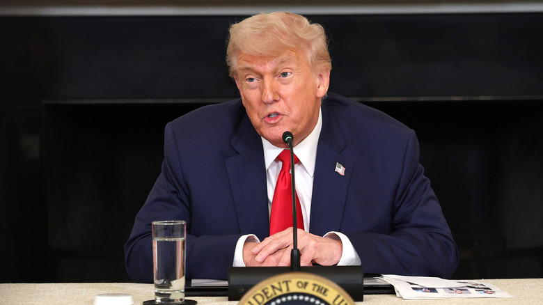 Donald Trump sits at a table in front of a microphone