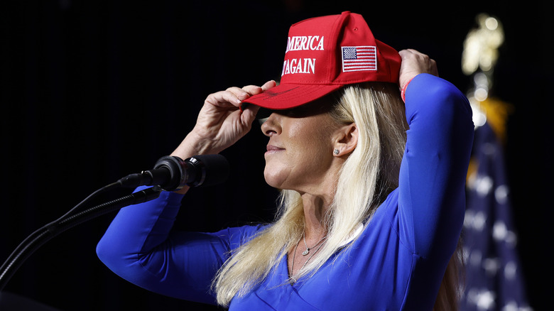 Marjorie Taylor Greene putting on a MAGA hat