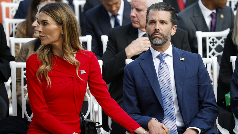 Bettina Anderson sitting next to Donald Trump Jr. in a red dress while holding his hand