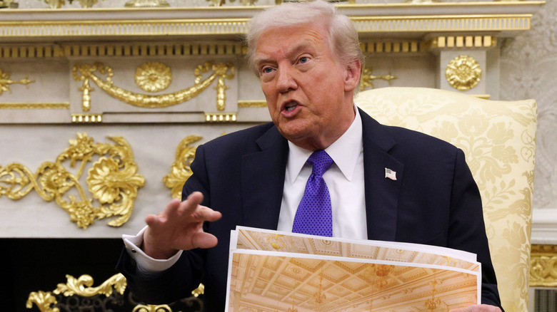 Donald Trump speaking while holding mockups of the White House ballroom
