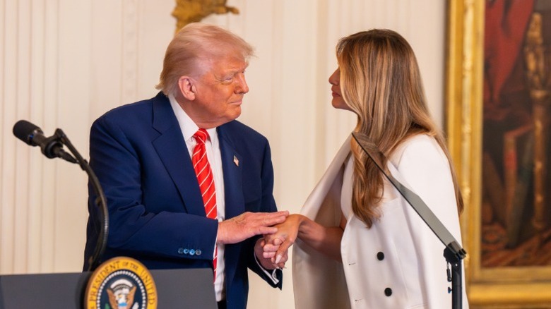 Donald Trump and Melania Trump hold hands onstage at an event in the East Room (2025)