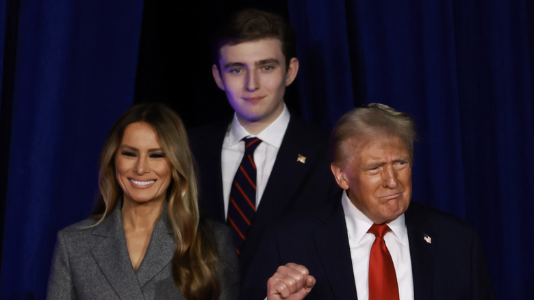 Donald Trump and Melania Trump standing in front of Barron Trump who's smirking in a suit at the Republican National Convention.