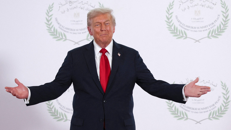 Donald Trump in Egypt with his arms outstretched in a black suit with a red tie