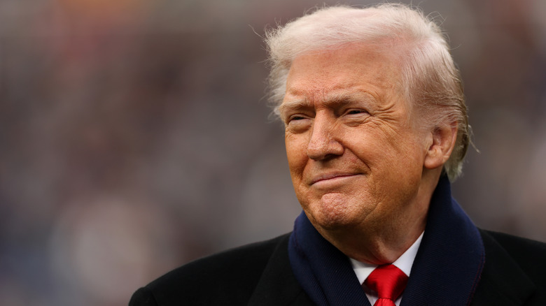 Donald Trump smiling in a black coat, outside