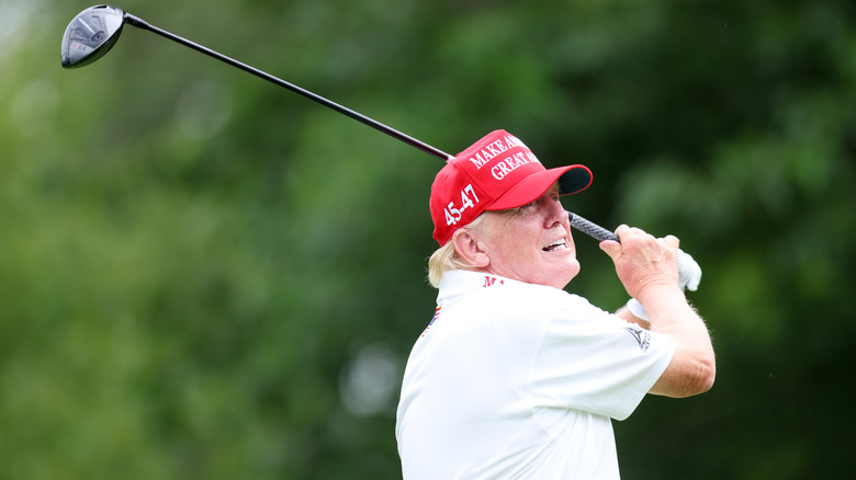 Donald Trump swinging a golf club in a red MAGA hat