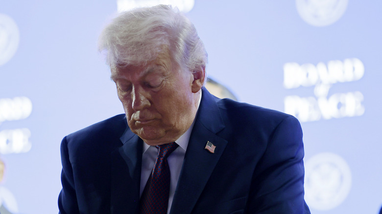 Donald Trtump eyes closed looking down at the Board of Peace in a navy suit with an American flag pin
