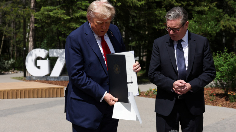 Donald Trump dropping papers as he tries to show off his signature while British Prime Minister Keir Starmer looks on