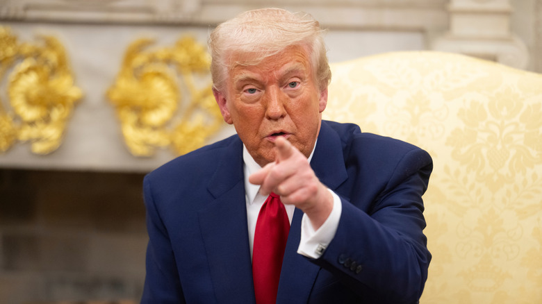Donald Trump pointing in a navy suit with a red tie while sitting in a gold chair