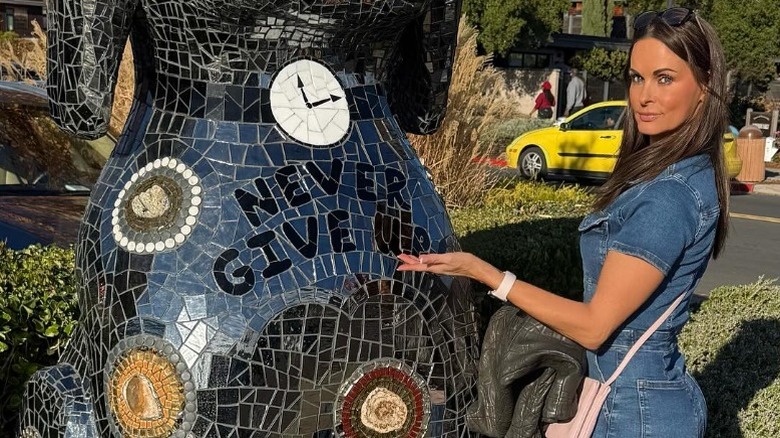 Karen McDougal points at a statue that reads 'Never give up' (2024)