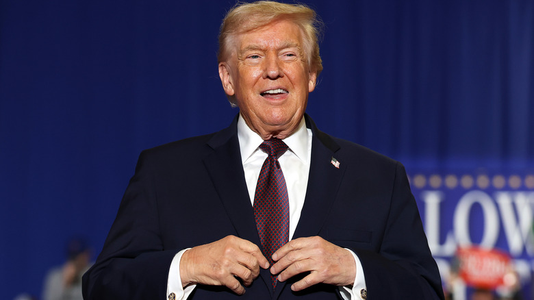 Donald Trump grinning while holding his fingers together in a black suit