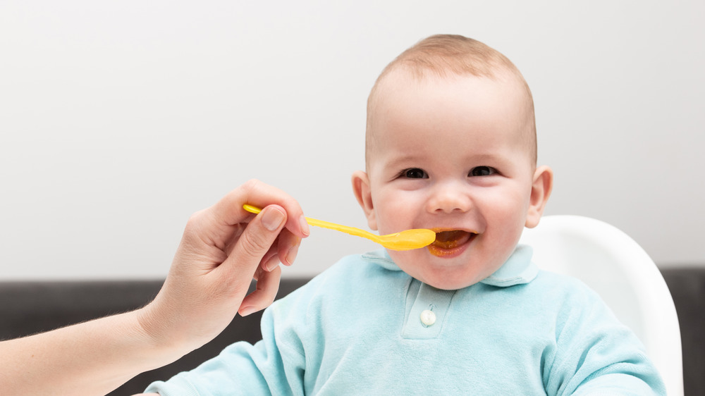 A hand feeding a baby a spoonful of food 