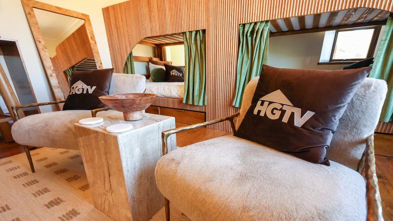 Promo photo of an HGTV collaboration (cream chairs with brown HGTV pillows and green curtains) with "The Bachelor" franchise in 2026.