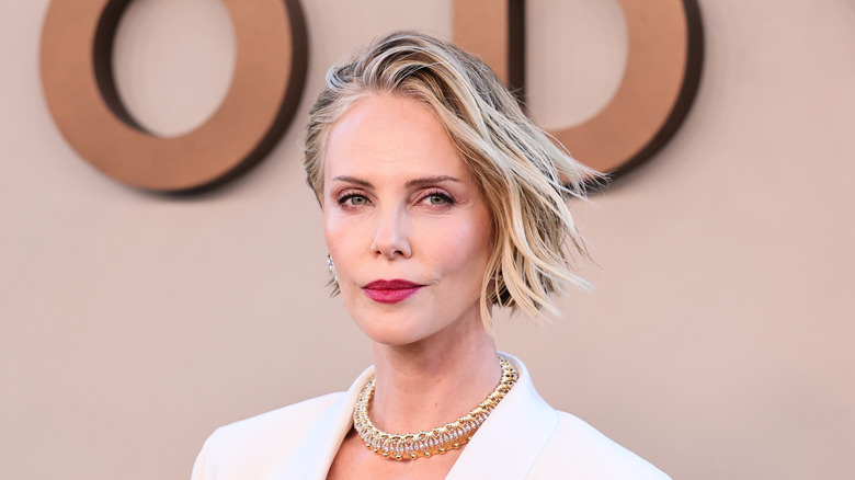 Charlize Theron sporting short hair and white blazer with gold jewelry