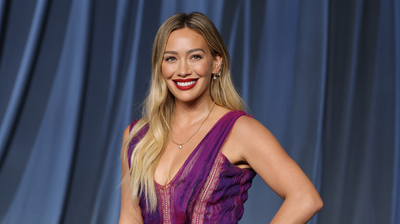 Hilary Duff smiling in a printed purple dress against blue background
