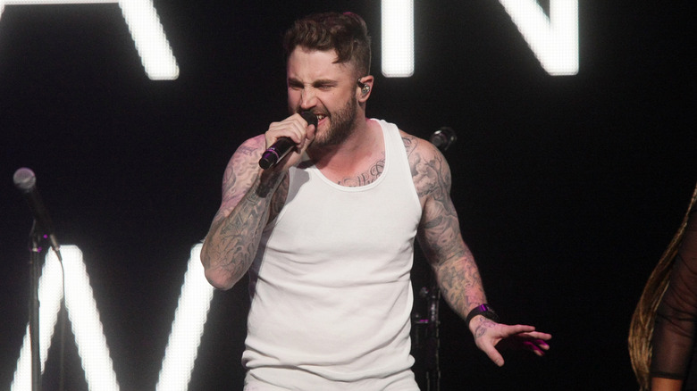 Dr. Phil's son Jordan McGraw sings into a microphone on stage in a white tank