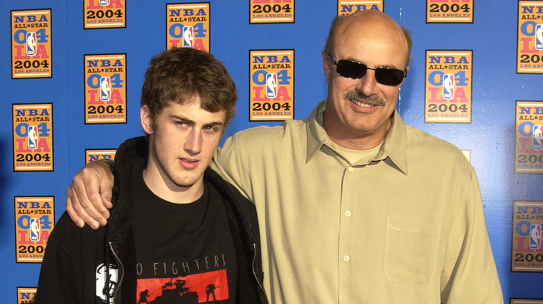Dr. Phil wears sunglasses smiling on the red carpet next to his teenage son Jordan.