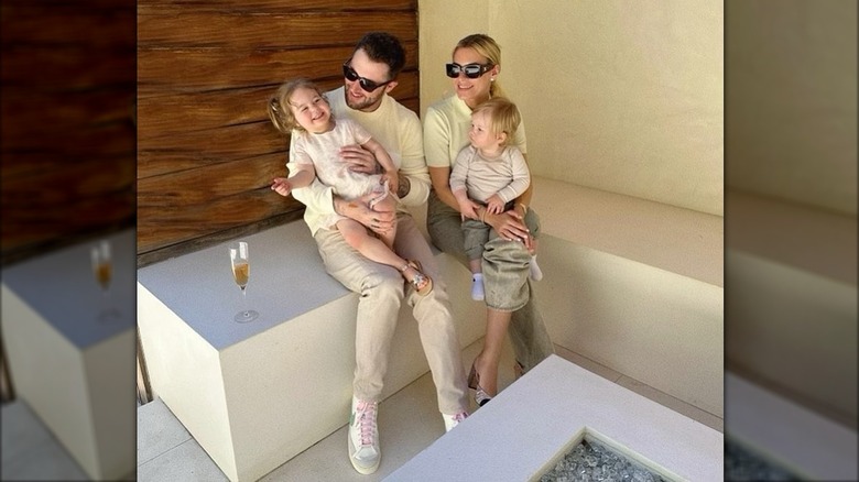 Jordan McGraw kisses his wife while they hold their two toddlers sitting outside.