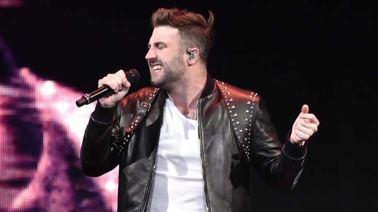 Jordan McGraw wears a leather jacket on stage singing into a microphone