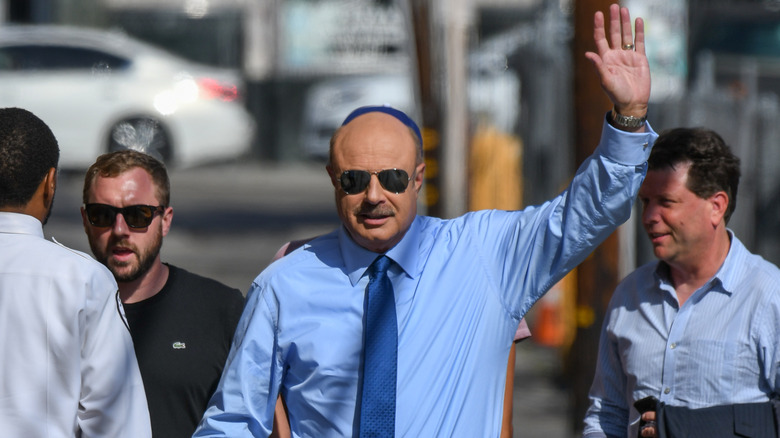 Phil McGraw raising his hand while walking down a street