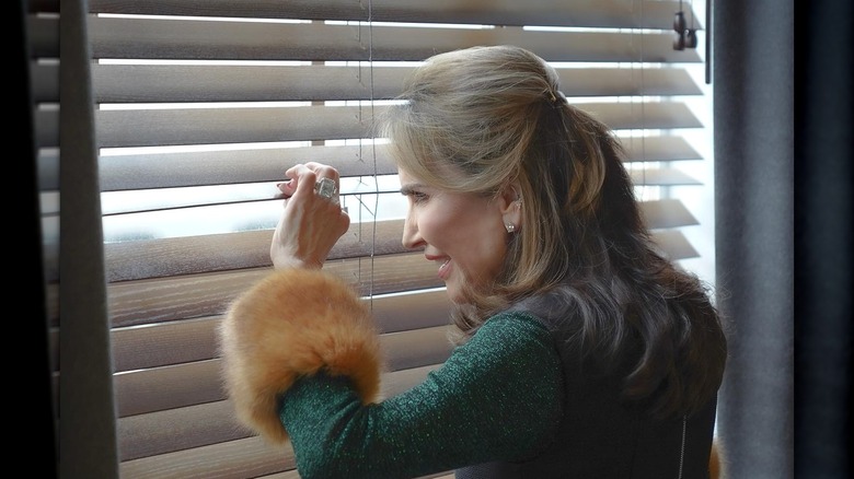 Robin McGraw looking through blinds green jacket fur cuffs
