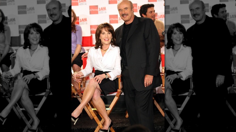 Robin McGraw sitting cross-legged while Phil McGraw stands with his arm around her