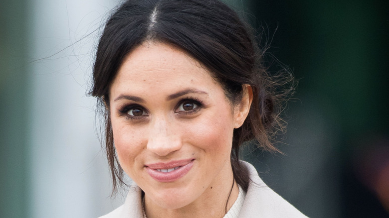 Meghan Markle smiles wearing a bun in her hair
