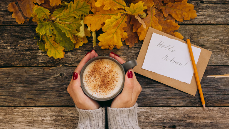 hands holding mug with 'Hello Autumn!' sign