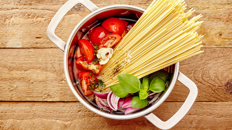 dried pasta in a pot with tomatoes, onions, and basil