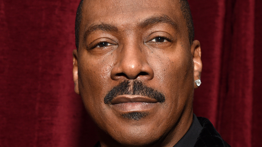 Eddie Murphy with slight grin, mustache and diamond earring