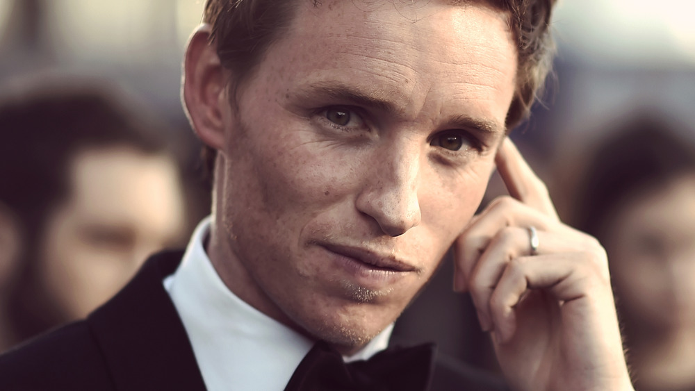 Eddie Redmayne holding a finger to his temple 