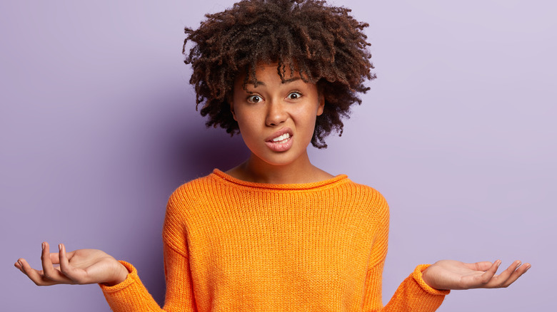 Woman wearing orange sweater shrugging her shoulders.