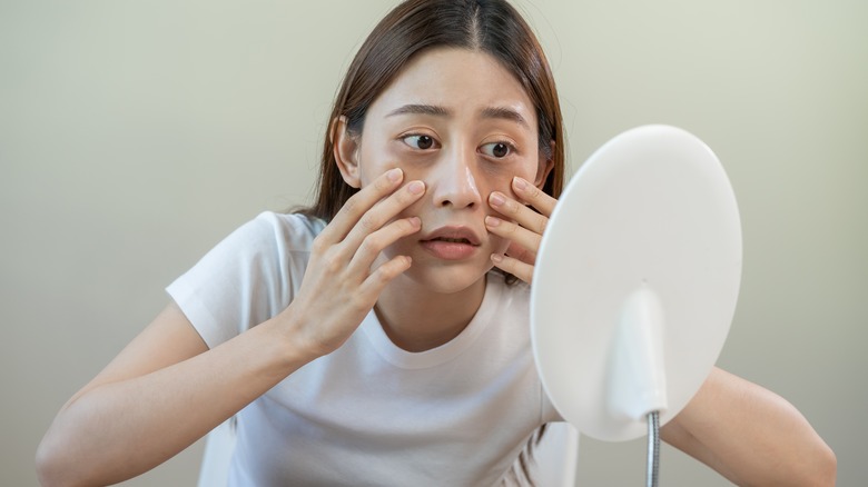 Woman looking in mirror hands on cheeks