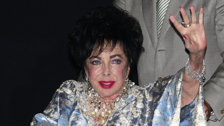 Elizabeth Taylor in wheelchair waving hand