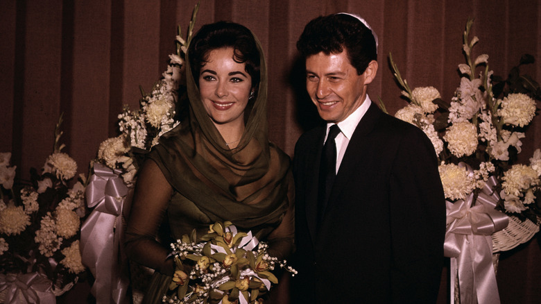 Eddie Fisher and Elizabeth Taylor getting married at a Jewish temple with flowers behind them