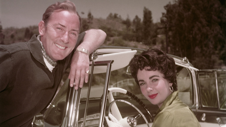 Michael Wilding posing next to Elizabeth Taylor behind the wheel
