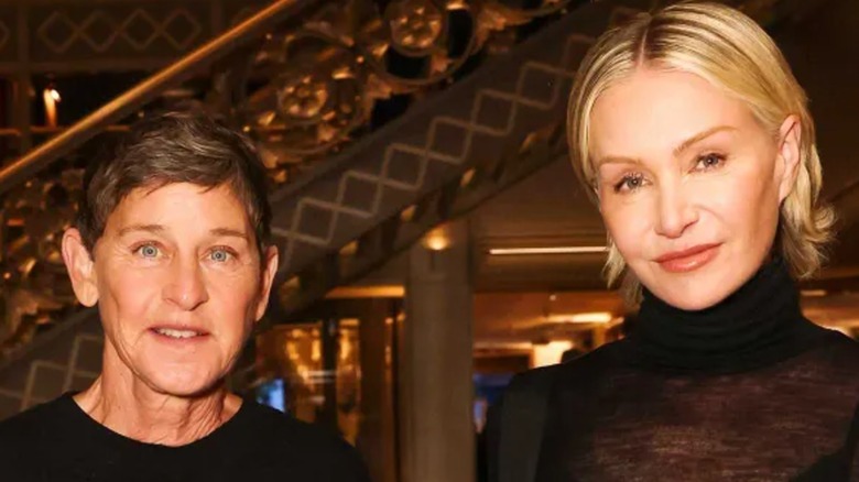Ellen DeGeneres and Portia de Rossi both wearing black and standing in front of a staircase