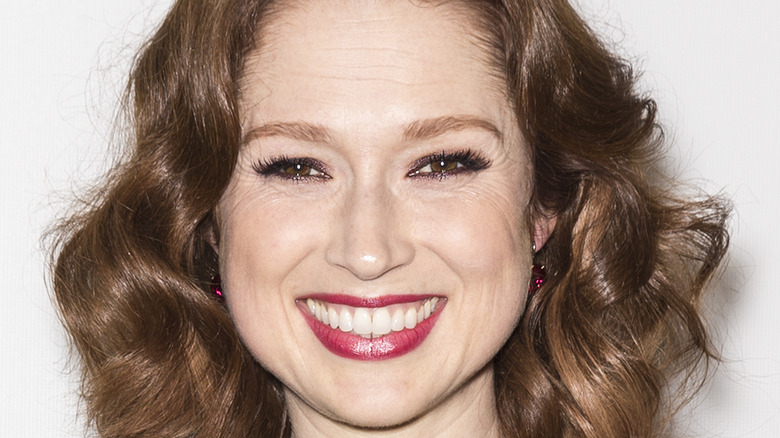 Ellie Kemper smiles with red lips and curly hair.