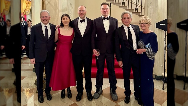 Elon Musk wearing a tuxedo and oversized sneakers in a group photo with others wearing formal wear