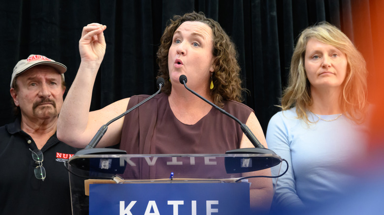 Katie Porter talking into a microphone with her hand raised and ehr mouth open.