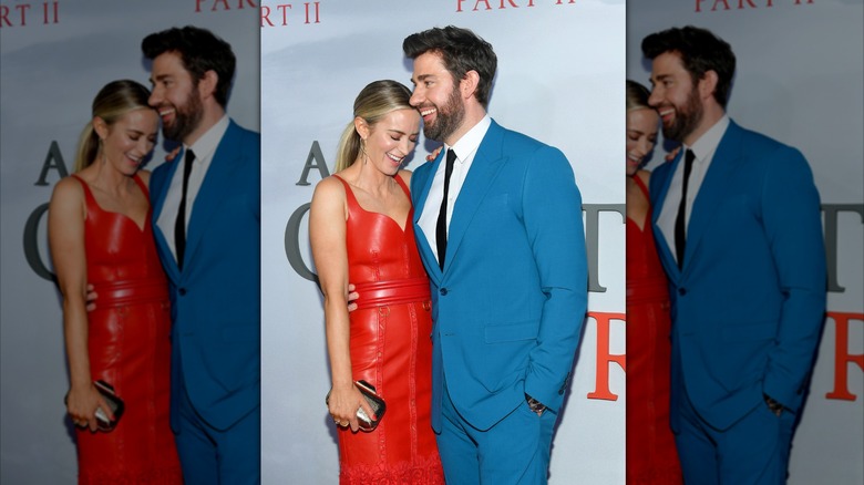 Emily Blunt in a red dress stands by John Krasinski in blue