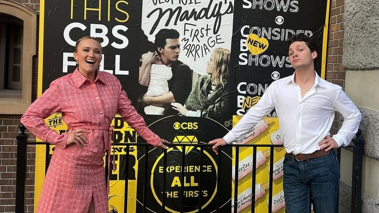Emily Osment and Montana Jordan posing in front a poster of "Georgie & Mandy's First Marriage"
