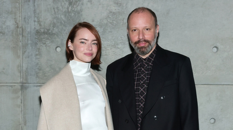 Emma Stone and Yorgos Lanthrimos posing for a picture together in front of a distressed concrete wall