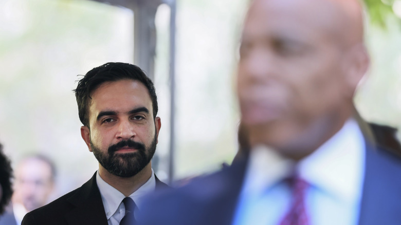 An out-of-focus Eric Adams with an in-focus Zohran Mamdani standing behind him