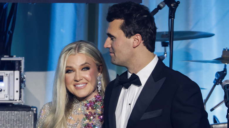 Erika Kirk in a white dress looking straight ahead while holding hands with husband, Charlie Kirk.