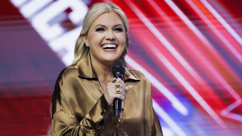 Erika Kirk holding mic smiling gold satin shirt